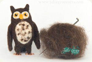 A needle felted owl sculpture next to the raw fleece and needle used